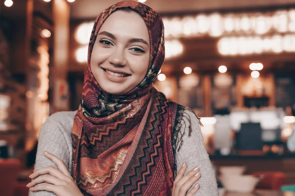 Aranyos bájos Arab lány a fejkendő a fején néz a kamerába, és mosolyogva ül egy kávézóban — Stock Fotó