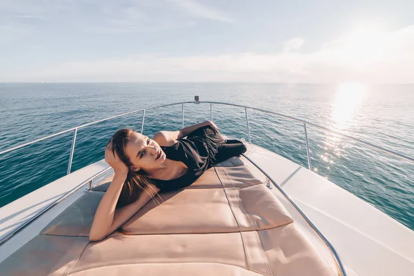 A luxurious girl in stylish black clothes lies on her yacht in the sun, resting — Stock Photo, Image