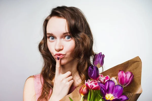 Divertente bella ragazza dagli occhi azzurri in posa con un grande mazzo di fiori, mettere un dito alle labbra — Foto Stock