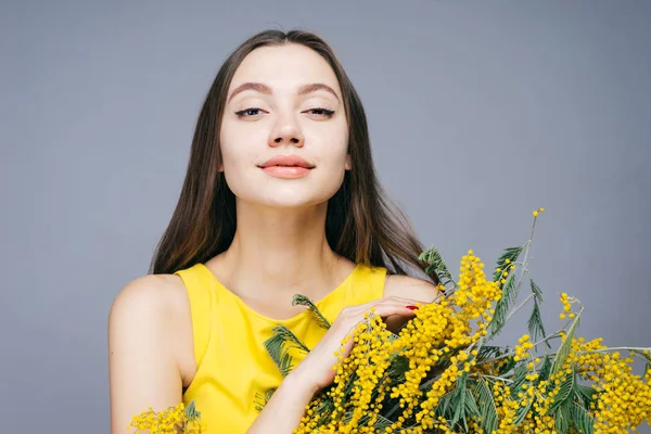 Confiada hermosa chica posando, mirando a la cámara, sosteniendo un ramo de mimosa amarillo primavera — Foto de Stock