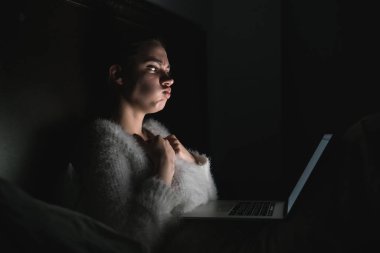 pijama korkmuş genç kız yatakta gece geç saatlerde, laptop korku filmi izlerken oturur