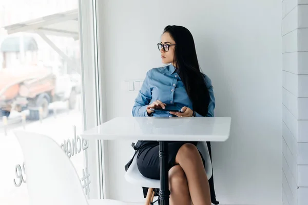 Jovem morena elegante em freelancer em camisa azul e óculos senta-se no café e pensa sobre o trabalho — Fotografia de Stock