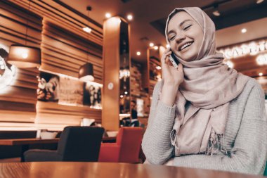 güzel bir rahat restoranda telefonda konuşurken başında başörtüsü ile gülen genç Arap kız