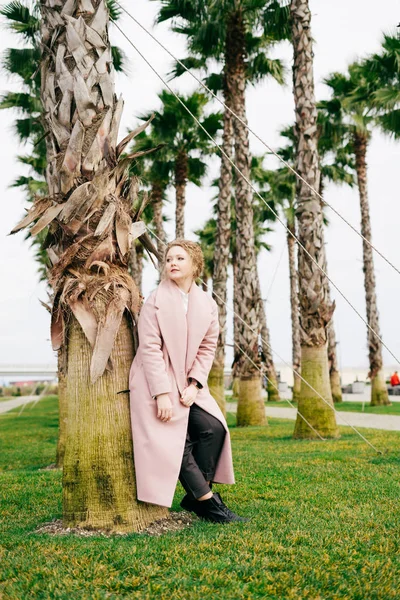 나무, 봄, 온 근처 공원에서 포즈 핑크 코트에 우아한 세련 된 여자 — 스톡 사진