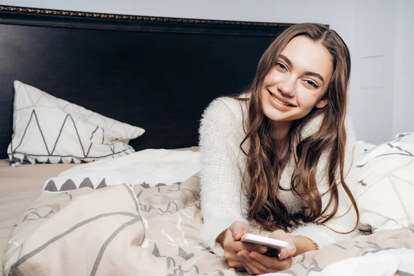 Charmante jonge meisje in witte pyjama liggend op bed, rust en glimlachen — Stockfoto