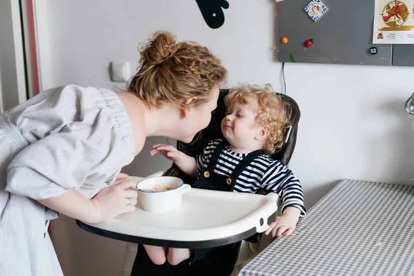 Curly young mother feeds her little son child, have fun and laugh — Stock Photo, Image