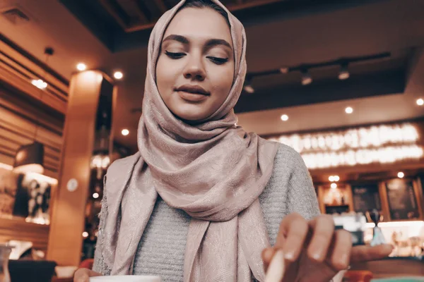 Gyönyörű Arab lány hidzsáb étteremben ül, és eszik a finom étel, mosolyogva — Stock Fotó
