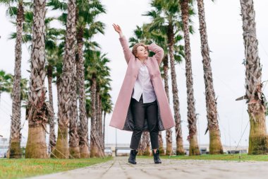 pembe bir ceket mutlu etkin kız yürüyor yeşil bahar parktan ellerini yukarı doğru kaldırdı