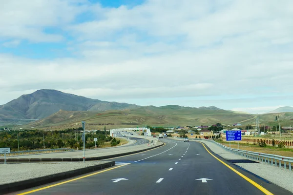 A flat road near the mountain slopes and hills below the cloudy sky, the magical nature — Stock Photo, Image