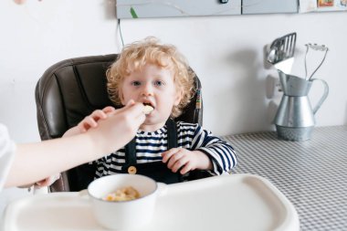 Küçük kıvırcık mavi gözlü çocuk mutfakta annesiyle sağlıklı yemek yeme