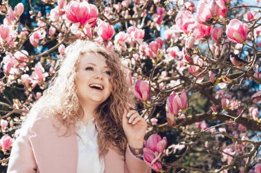 kıvırcık saçlı gülen kadın bahar ve sıcaklık parkta güneşin tadını pembe bir ceket