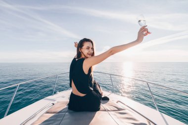 siyah yaz giysileri mutlu güzel kız beyaz bir yatta oturur, deniz yolculuğu sahiptir, şampanya içiyor