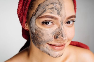 Sevimli Genç kız gülümsüyor, yarım yüz kil maskesi başında kırmızı bir havlu ile