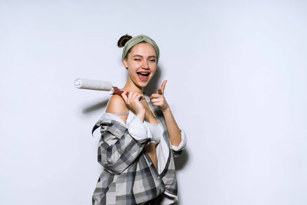Grappige meisje in een plaid shirt doen van reparaties in haar appartement, bedrijf van een roller voor het schilderen van de muren — Stockfoto
