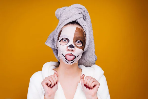 Drôle jeune fille avec une serviette sur sa tête montrant la langue, sur le visage un masque avec masque d'un chien — Photo