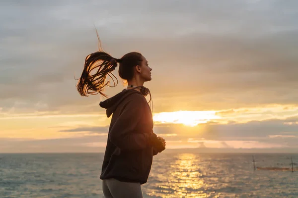 Persistente ragazza dai capelli lunghi in un maglione corre lungo il lungomare al tramonto — Foto Stock