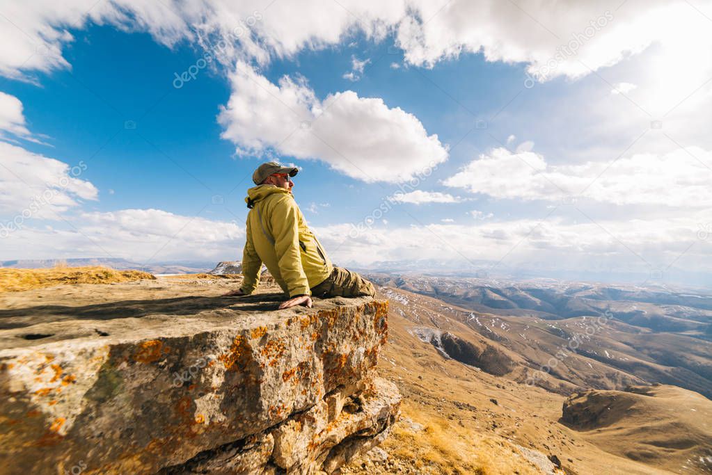 male traveler in a bright warm jacket enjoying the mountain scenery and the sun