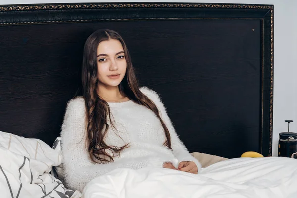 Encantadora chica somnolienta con el pelo largo sentado en la cama tarde en la noche, descansando y queriendo dormir — Foto de Stock