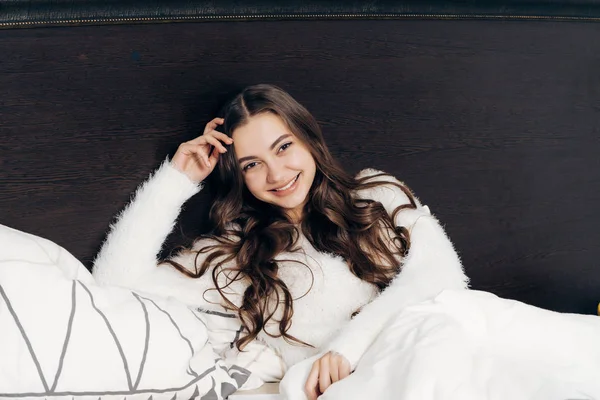 Menina feliz em pijama branco jaz na cama, bom humor e manhã — Fotografia de Stock