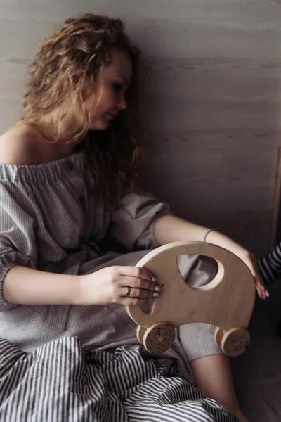 Σγουρά νεαρή γυναίκα σε ένα φόρεμα ένα ξύλινο παιχνίδι κρατά στα χέρια της — Φωτογραφία Αρχείου