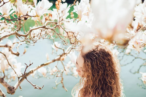 Chica de lujo de pelo rizado disfrutando del aroma de magnolia en el parque, ama el sol y la calidez — Foto de Stock