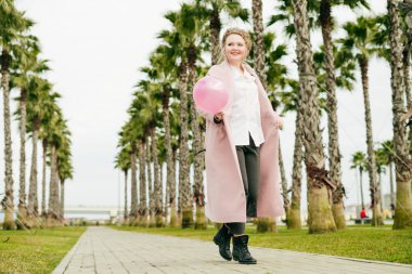 pembe bir ceket lüks zarif kadın parkta yürüyor ve eğlence var, bir pembe balon tutar