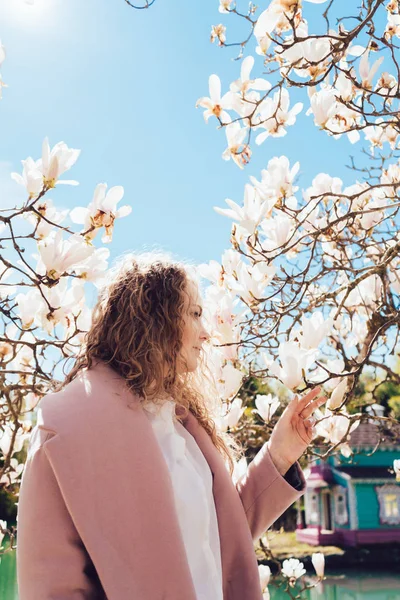 Elegant curly woman enjoys fragrant magnolia under the blue sky, warm spring weather — Stock Photo, Image