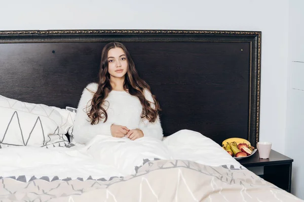 Niña somnolienta en pijama blanco descansando en la cama por la noche, quiere dormir — Foto de Stock