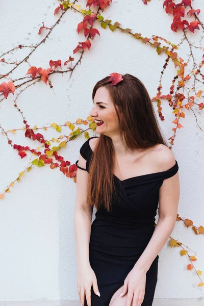 Mujer de pelo largo de lujo en un hermoso vestido negro posando contra la pared y riendo — Foto de Stock