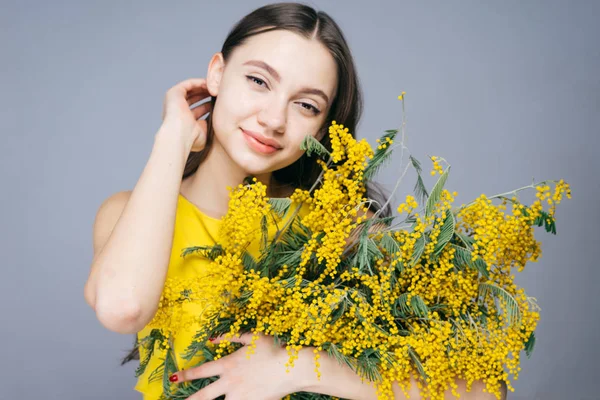 Happy young girl enjoys the warmth, holds in her hands a fragrant yellow mimosa — Stock Photo, Image