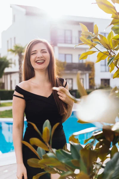 Lussuosa donna attraente dai capelli lunghi in un vestito nero ridere, su uno sfondo blu piscina — Foto Stock