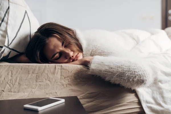 Niedliches junges Mädchen im weißen Schlafanzug, das frühmorgens auf dem Bett schläft, kann den Wecker nicht hören — Stockfoto