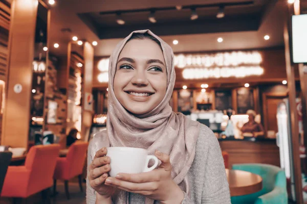 Bájos muszlim nő hidzsáb italok illatos kávé a hangulatos kávézót és mosoly — Stock Fotó