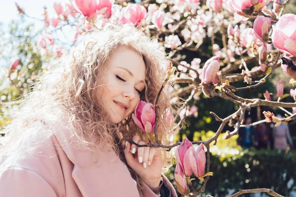 Chica elegante rizado disfruta de la calidez y el aroma de magnolia en el parque — Foto de Stock