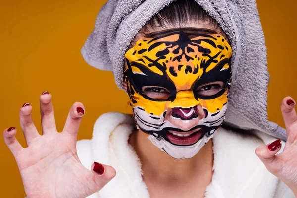 Una giovane ragazza divertente con un asciugamano sulla testa ringhia come una bestia, sul suo viso una maschera idratante con un viso leopardato — Foto Stock