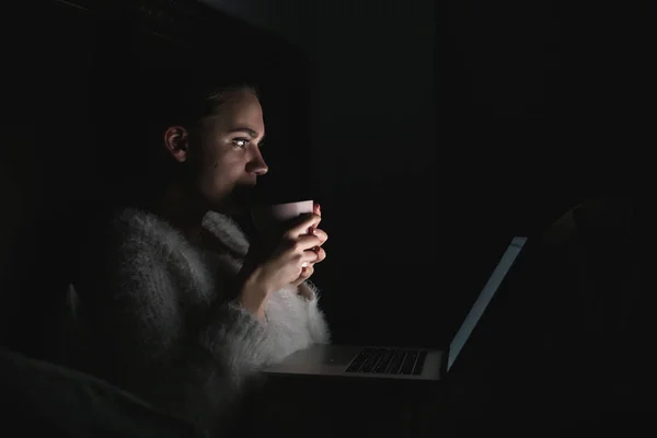 Gece geç saatte yatakta otururken, çay içme ve dizüstü bilgisayarda Tv dizi izlemek genç kız odaklı — Stok fotoğraf