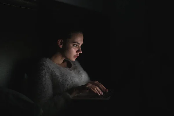 Sonnolenta giovane ragazza seduta a letto a tarda notte guardando un film sul suo computer portatile — Foto Stock