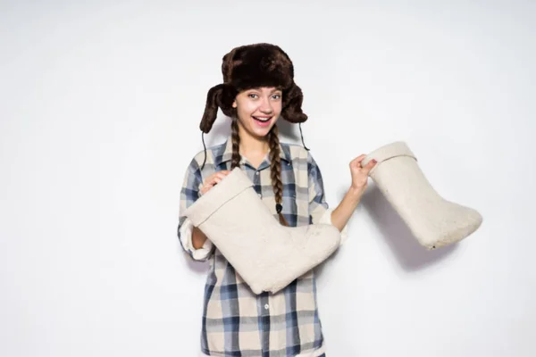 A joyful young Russian girl with pigtails in a warm fur hat rejoices in the winter, holds the gray felt boots in her hands — Stock Photo, Image