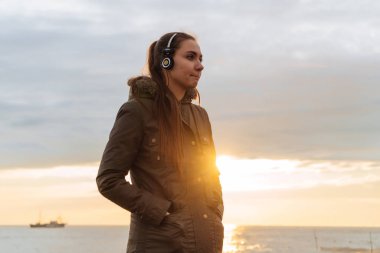 Sevimli Genç kız sıcak ceket deniz manzaralı kulaklıklar müzik dinlemek sahiptir