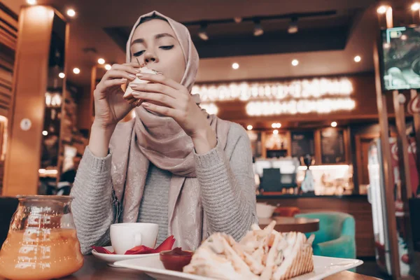 Молодая мусульманка с платком на голове обедает в уютном ресторане, вкусной едой и ароматным чаем — стоковое фото