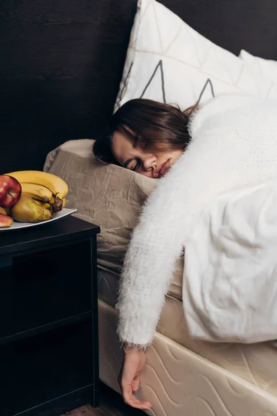 Ein junges langhaariges Mädchen im weißen Pyjama schläft im Bett, will morgens nicht aufstehen — Stockfoto