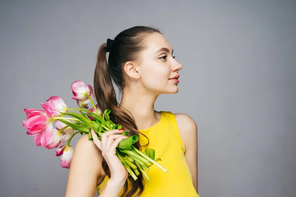 Confident attractive woman in yellow dress holds bouquet of flowers and poses — Stock Photo, Image