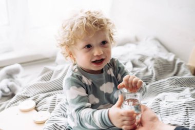 komik sarışın kıvırcık saçlı bebek çocuk oturur yatak ve gülümsüyor, İçecek su