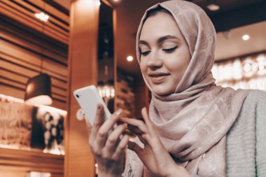 bir başörtüsü başında bir güzel Arap kızla yemeğini restoranda bekliyor, telefonda bir ileti yazar