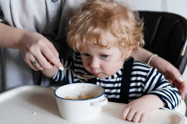 küçük bir kıvırcık saçlı çocuk annesinin yanında, sağlıklı ve lezzetli bir yemek yemek kahvaltı