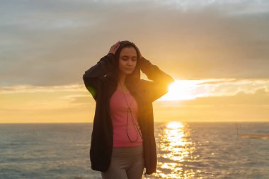 Bir genç atletik kız deniz kenarında günbatımında koşu önce güç kazanıyor