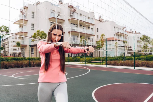 Menina atlética confiante em uma jaqueta rosa posando contra uma rede de voleibol em um playground — Fotografia de Stock