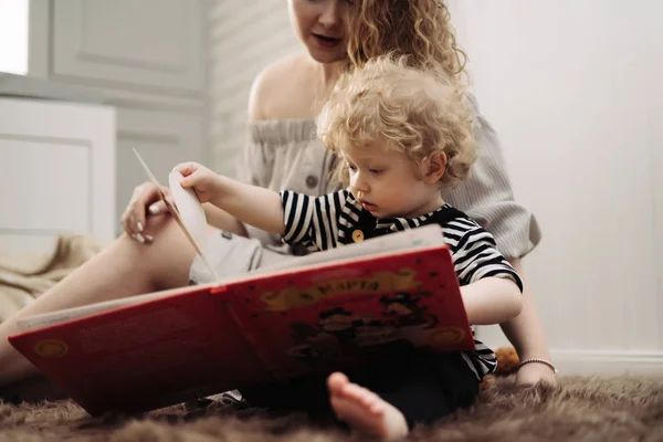 Little curly baby boy sitting with mom on the floor learning to read — Stock Photo, Image