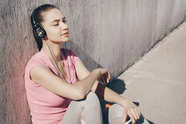 Calma giovane ragazza in t-shirt rosa si siede a terra ascoltando musica sulle cuffie — Foto Stock