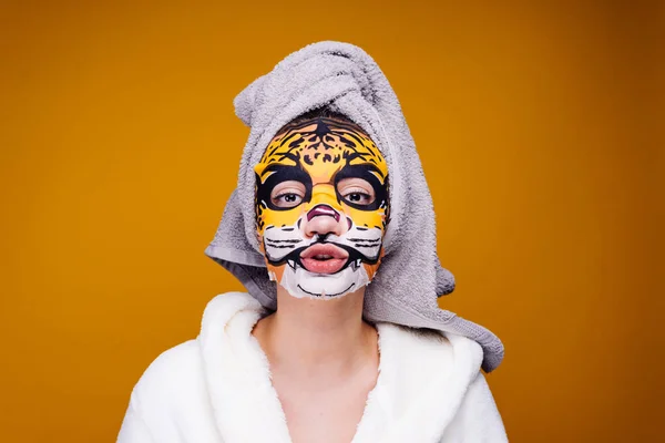 Krásná dívka s bílým ručníkem na hlavě a v košili vypadá do kamery, na její tváři hydratační maska s tváří leopard — Stock fotografie